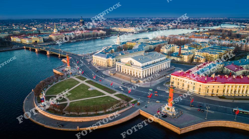 а снимке изображена Стрелка Васильевского острова — одна из знаковых достопримечательностей Санкт-Петербурга. Центральное место занимает здание Биржи, выполненное в классическом стиле, окруженное Ростральными колоннами. Река Нева и архитектура исторического центра дополняют композицию, подчеркивая уникальность этого места. Утренний свет создает мягкие оттенки и гармонию пейзажа.